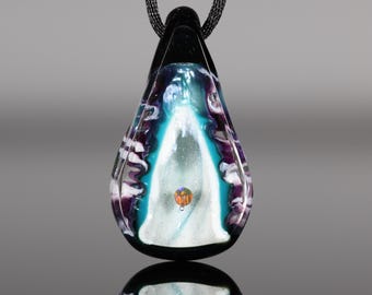 May include: A teardrop-shaped pendant with a black top and a colorful design. The pendant features shades of teal, purple, and white, with a small orange accent. It hangs from a black chain.