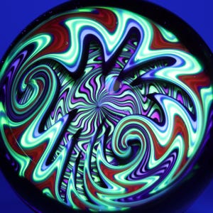 May include: A glass marble with a swirling, psychedelic design. The marble features a central spiral of green and purple, surrounded by red, blue, and green wavy patterns. The background is a deep blue.