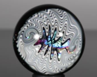 May include: A black glass marble with a swirling white pattern and a central iridescent design. The marble is round and sits on a small black base. The iridescent design features shades of blue, purple, and green.