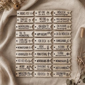 May include: A collection of thirty rectangular wooden gift tags arranged in three columns. Each light-colored wooden tag features a hole on the left side and various black printed holiday-themed phrases and icons, including stars, hearts, gifts, and trees.