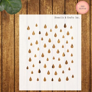 May include: A white stencil with a repeating pattern of raindrops. The stencil is on a wooden background. The text "Stencils & Crafts Inc." is printed at the top of the stencil.