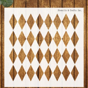 May include: A square white stencil sheet featuring a repeating pattern of diamond shapes arranged in a grid. The text Stencils & Crafts Inc. is printed in the upper right corner. The stencil is displayed against a vertical brown wood grain background.