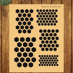 May include: A tan stencil sheet with multiple black honeycomb patterns. The stencils are in various sizes and arrangements. The text "Stencils & Crafts Inc." is printed at the top. The background is a wooden surface.