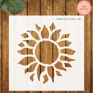 May include: White sunflower stencil with a detailed design. The stencil is on a white background with the text "Stencils & Crafts Inc." The background is a wooden surface.