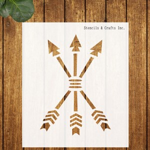 May include: A white rectangular stencil featuring a cutout design of three crossed arrows bound together in the center. The arrows point both upward and downward with detailed fletching at the ends. The text Stencils & Crafts Inc. is visible.