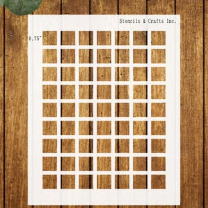 May include: White stencil with a grid pattern of evenly spaced squares. The stencil is labeled "0.75" on the left side and "Stencils & Crafts Inc." at the top right. The stencil is placed on a wooden surface.