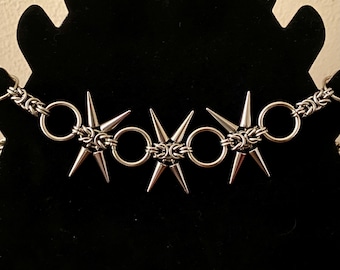 May include: A silver chain necklace with multiple pointed star-shaped charms. The necklace is on a black background.