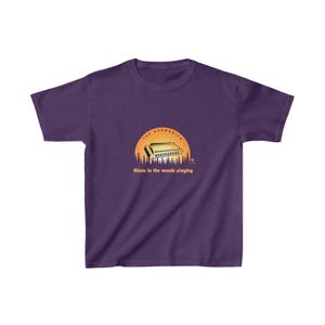 May include: A purple t-shirt with a graphic of a harmonica set against a sunset and trees. The text reads "THE HARMONICA" and "Alone in the woods playing". The shirt is made of a soft material. A musical themed t-shirt.