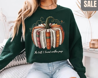 May include: Forest green sweatshirt featuring a pumpkin design made of books. The pumpkin has a green stem and is surrounded by open books in shades of orange, red, and brown. The text "The Fall I Turned another page" is below the pumpkin.