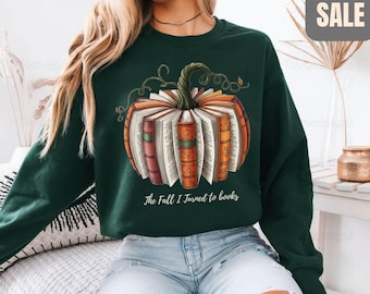 May include: Forest green sweatshirt featuring a pumpkin design made of books. The pumpkin has a stem and vines. The text "The Fall I Turned to Books" is below the pumpkin. The word "SALE" is in a gray box in the upper right corner.