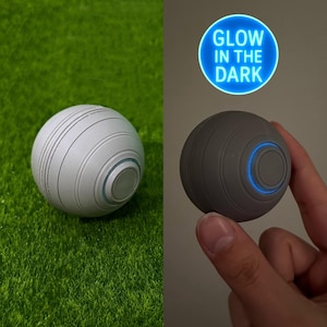 May include: A gray, spherical object with a circular design and a glowing blue light. The object is shown in two states: one in daylight and the other glowing in the dark. The text "GLOW IN THE DARK" is displayed in a blue circle.