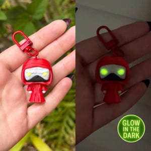 May include: Red glow-in-the-dark keychain featuring a character with a hooded robe and glowing eyes. "GLOW IN THE DARK" is written on the image.