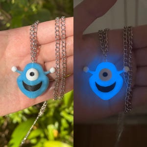 May include: A blue glow-in-the-dark necklace with a one-eyed monster pendant. The pendant has a black mouth and white eyes.