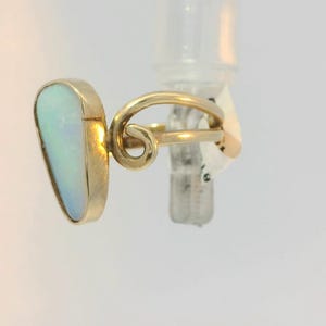 May include: A gold ring with a white opal gemstone. The ring has a unique, twisted band.