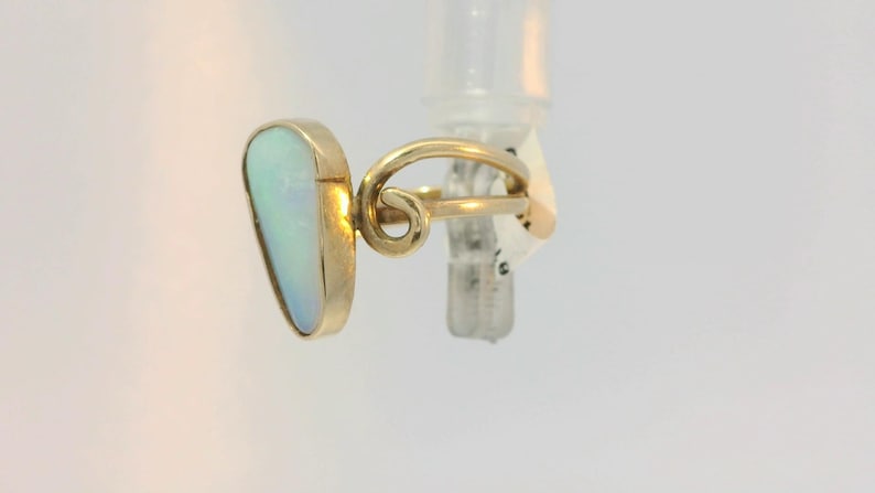 May include: A gold ring with a white opal gemstone. The ring has a unique, twisted band.