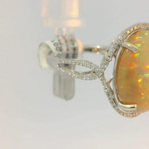 May include: A white gold ring with a large oval opal gemstone surrounded by a halo of small diamonds. The ring has a delicate, intricate design.