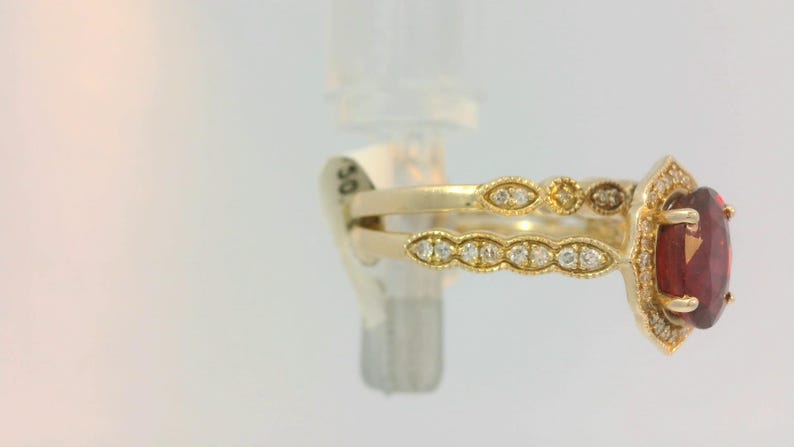 May include: A gold ring with a large red gemstone surrounded by smaller diamonds. The ring is set on a white background.