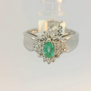 Pu&ograve; includere: Un anello d'argento con uno smeraldo verde circondato da diamanti pi&ugrave; piccoli.