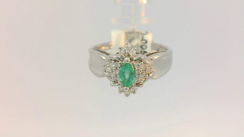 Pu&ograve; includere: Un anello d'argento con uno smeraldo verde circondato da diamanti pi&ugrave; piccoli.
