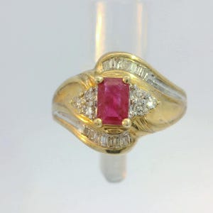May include: A gold ring with a red ruby gemstone and smaller diamonds set in a wavy band.