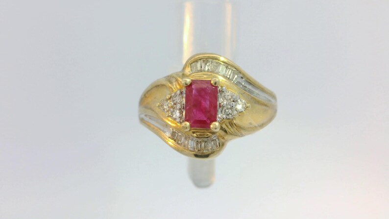May include: A gold ring with a red ruby gemstone and smaller diamonds set in a wavy band.