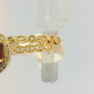 May include: A gold ring set with a large oval-shaped red gemstone surrounded by smaller diamonds. The ring is paired with a matching band featuring a row of diamonds set in a delicate design.