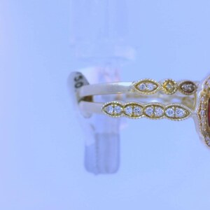 May include: A gold ring with a large red gemstone surrounded by smaller diamonds. The ring has a delicate, intricate design.