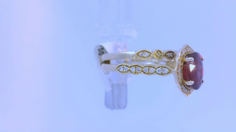 May include: A gold ring with a large red gemstone surrounded by smaller diamonds. The ring has a delicate, intricate design.