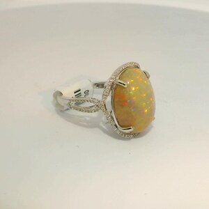 May include: A silver ring with a large oval-shaped opal gemstone set in a diamond halo. The ring has a delicate, twisted band.