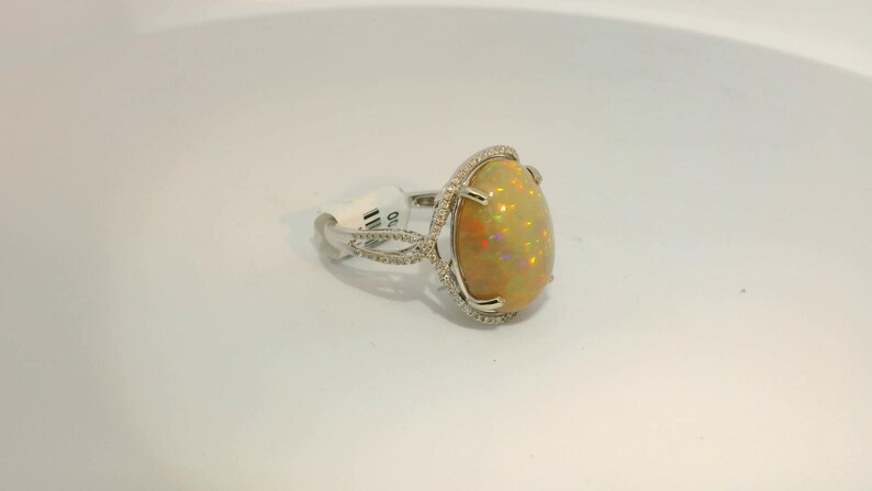 May include: A silver ring with a large oval-shaped opal gemstone set in a diamond halo. The ring has a delicate, twisted band.