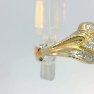 May include: A gold ring with a red gemstone and small diamonds. The ring has a detailed design with a curved band.