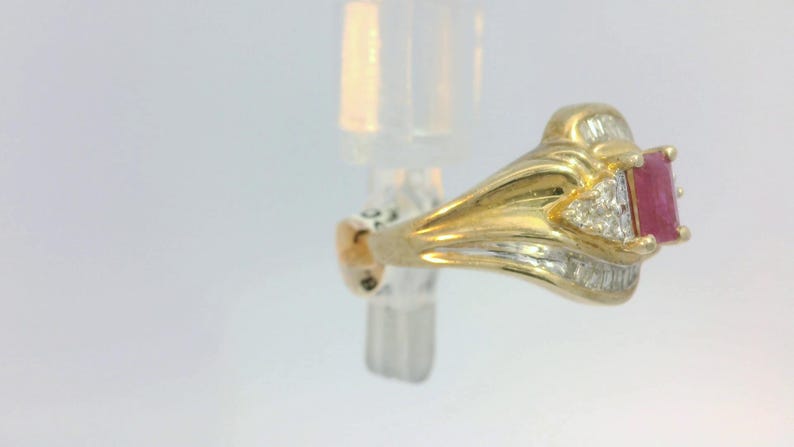 May include: A gold ring with a red gemstone and small diamonds. The ring has a detailed design with a curved band.