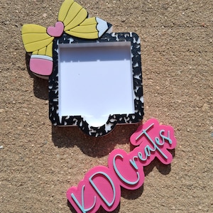 May include: A decorative pencil-themed frame with a black and white border, a white interior, and a yellow pencil design with a pink eraser and heart. The image also includes a pink sign with the text "KD Creates" in a light blue outline.
