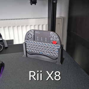 Puede incluir: Un teclado inalámbrico negro con un panel táctil integrado y un soporte. El teclado está etiquetado como "Rii X8".