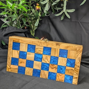 Op de afbeelding: Een houten schaakbord met blauwe en bruine vakjes. Het bord is gemaakt van olijfhout en heeft een natuurlijke afwerking.