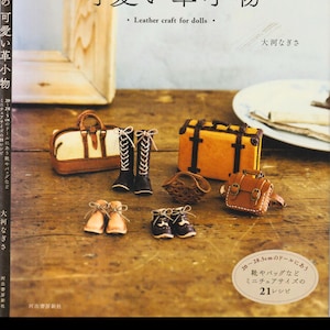 May include: A book cover in Japanese with the title "Cute Leather Goods for Dolls". The image displays miniature leather doll accessories, such as boots, shoes, a suitcase, and a handbag. The text "Leather craft for dolls" is also visible.
