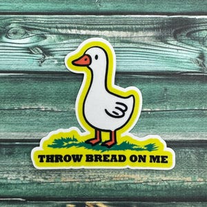 May include: A yellow and white sticker with a cartoon goose and the text "THROW BREAD ON ME".