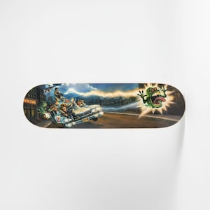 Puede incluir: Una patineta con una colorida ilustración de los Ghostbusters en su coche Ecto-1, persiguiendo a un fantasma verde. La obra de arte representa una ciudad y un rayo de energía. La patineta tiene una forma curva.