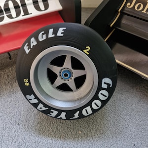 以下が含まれることがあります： 側面に「RR」と「2」の文字が書かれたグッドイヤーイーグルタイヤのクローズアップ。タイヤは黒地に白文字で、銀色のリムが付いている。