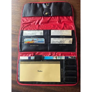 Puede incluir: Un organizador de viaje vintage negro y rojo con múltiples compartimentos. Cuenta con ranuras para tarjetas, notas y mapas, con el texto "Winter Driving Tips", "Highway Hints", "Gas Credit Card", "First Aid" y "Speed Limits". El organizador tiene un cierre a presión.