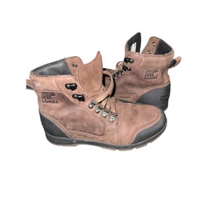 Könnte beinhalten: Braune wasserdichte Sorel-Stiefel aus Leder mit schwarzen Gummisohlen. Die Stiefel haben ein Schnürdesign mit Metallösen und das Sorel-Logo an der Seite. Für Outdoor-Aktivitäten konzipiert.