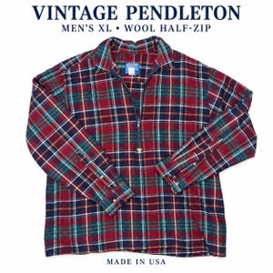 Peut inclure: Une chemise vintage Pendleton en laine à demi-fermeture éclair avec un motif à carreaux rouge, bleu marine et vert. Le vêtement comprend un col, des manches longues avec poignets boutonnés et une fermeture éclair centrale. Texte : VINTAGE PENDLETON MEN'S XL • WOOL HALF-ZIP MADE IN USA.