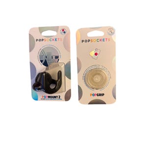 May include: Two packaged PopSockets products. On the left, a black PopMount 2 car vent mount. On the right, a clear, circular PopGrip phone stand with a swappable top. Both items are on branded cardboard backing with holographic circle patterns.