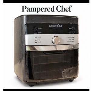 Puede incluir: Un horno freidora de aire Pampered Chef negro con un panel de control plateado. El frente cuenta con un dial central, una puerta de vidrio y etiquetas para configuraciones que incluyen Air Fry, Bake, Roast, Rotisserie, Reheat y Dehydrate.