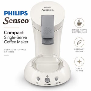 Könnte beinhalten: Eine cremefarbene Philips Senseo Kaffeepadmaschine mit einem grauen zentralen Verschlusshebel. Die Basis verfügt über drei runde Tasten mit Symbolen für eine Tasse, Strom und zwei Tassen. Der Text auf dem Bild enthält Philips Senseo.