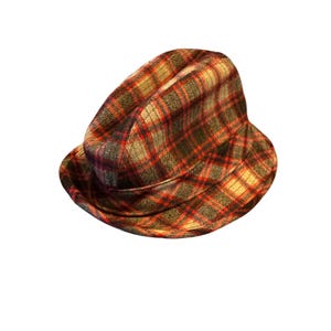 May include: A plaid fedora hat in shades of red, brown, and tan. The hat has a classic fedora shape with a slightly curved brim. The fabric has a textured appearance, and the hat is set against a white background.
