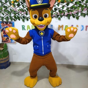 Könnte beinhalten: Ein Ganzkörperkostüm eines Cartoon-Hundcharakters mit blauer Polizeimütze und Uniform. Der Charakter hat ein gelbes Gesicht, braunes Fell und große Pfoten. Das Kostüm ist so gestaltet, dass es einem beliebten Zeichentrickcharakter ähnelt.