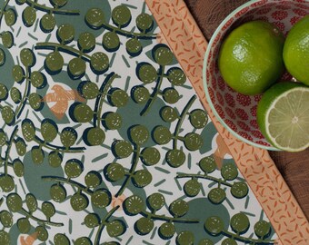 Könnte beinhalten: Ein gemustertes Küchentuch mit einem botanischen Design in Grün-, Blau- und Pfirsichtönen, zusammen mit einer Schüssel mit Limetten. Das Tuch hat ein sich wiederholendes Muster aus grünen Kreisen und Stielen. Die Schüssel hat ein rot-weißes Blumenmuster.