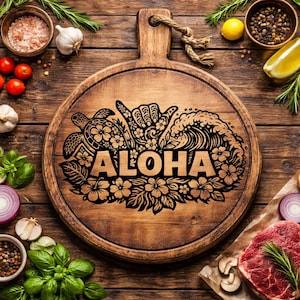 May include: A round wooden cutting board with a handle and rope detail. The board features a carved design with the word "ALOHA", a turtle, a hand gesture, and floral and wave elements. The board is surrounded by fresh ingredients like tomatoes, garlic, and herbs.