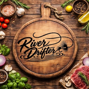 May include: A round wooden cutting board with a handle and the words "River Drifter" in black script. The board is surrounded by fresh ingredients like tomatoes, garlic, and herbs, suggesting a culinary theme.
